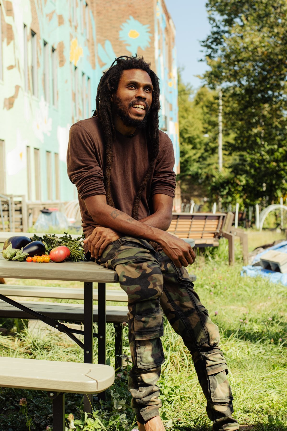 Farmer D sitting at the Armory Community Garden, smiling toward the camera.